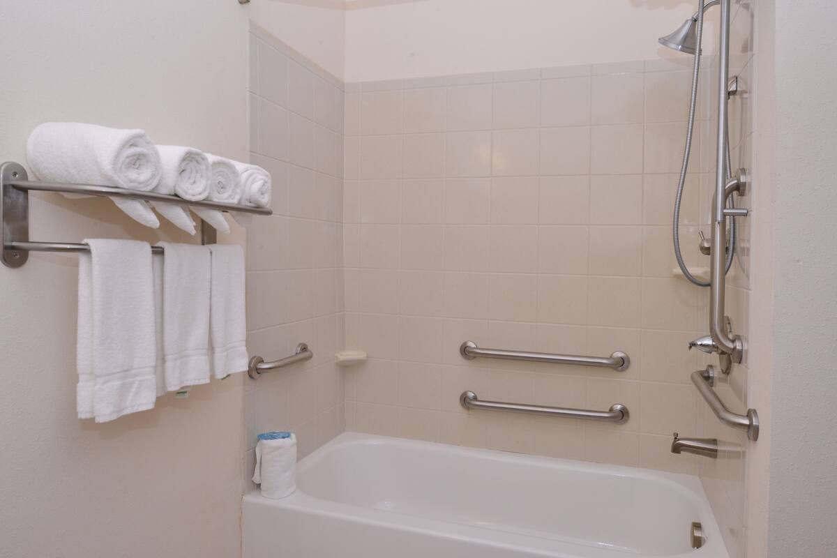 A bathroom with a bathtub, handrails, and a towel rack with folded towels.