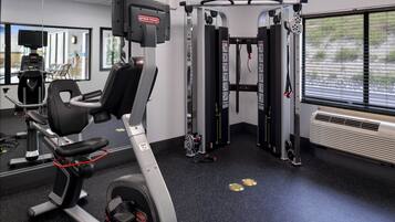 Ein Fitnessraum mit Trainingsgeräten, einer Spiegelwand und einem Fenster mit Jalousien.