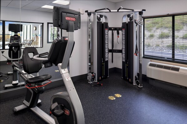 Un gimnasio con equipo de ejercicio, un espejo grande y una ventana con persianas.