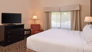 A hotel room with a large bed, a flat-screen TV on a dresser, a chair, and a window with curtains.