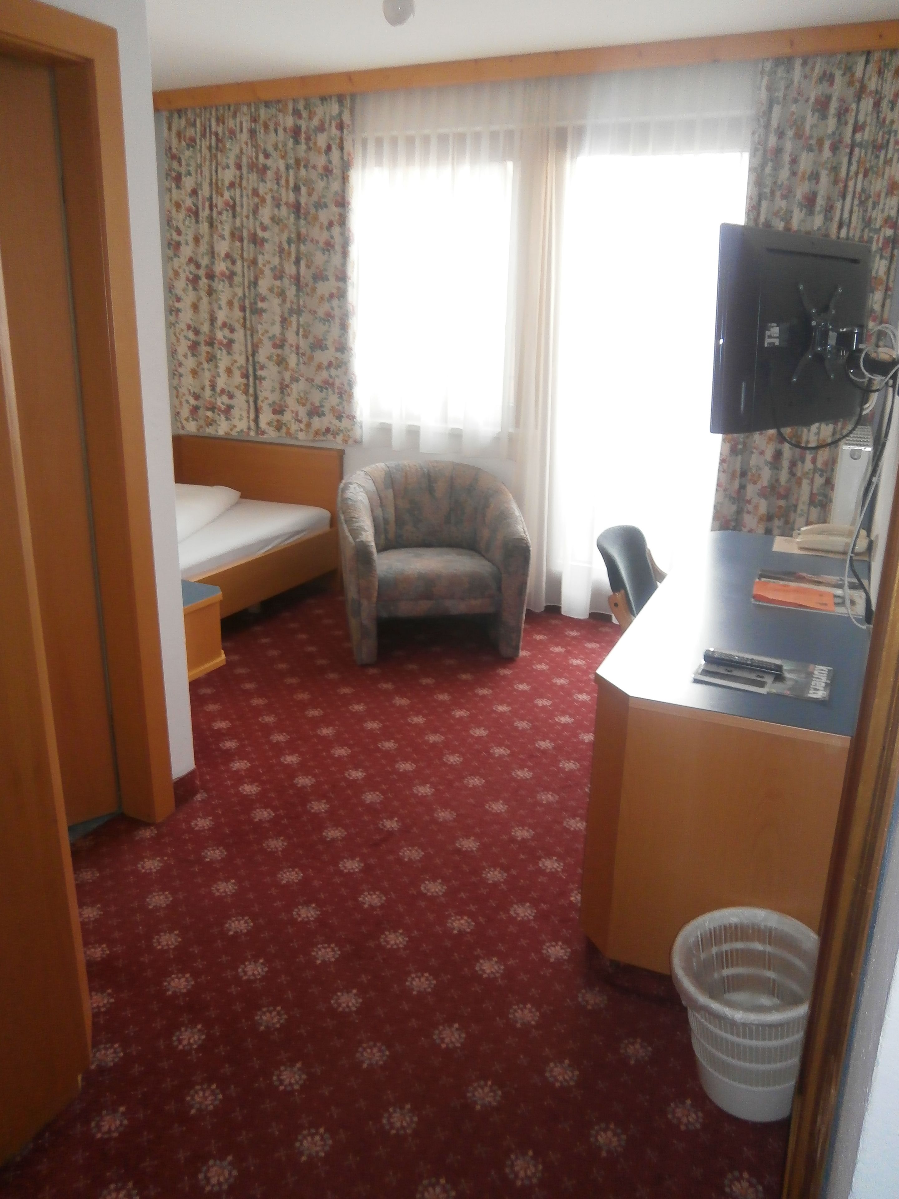 Une chambre d’hôtel avec un lit, une chaise, un bureau avec un ordinateur et une fenêtre avec des rideaux.