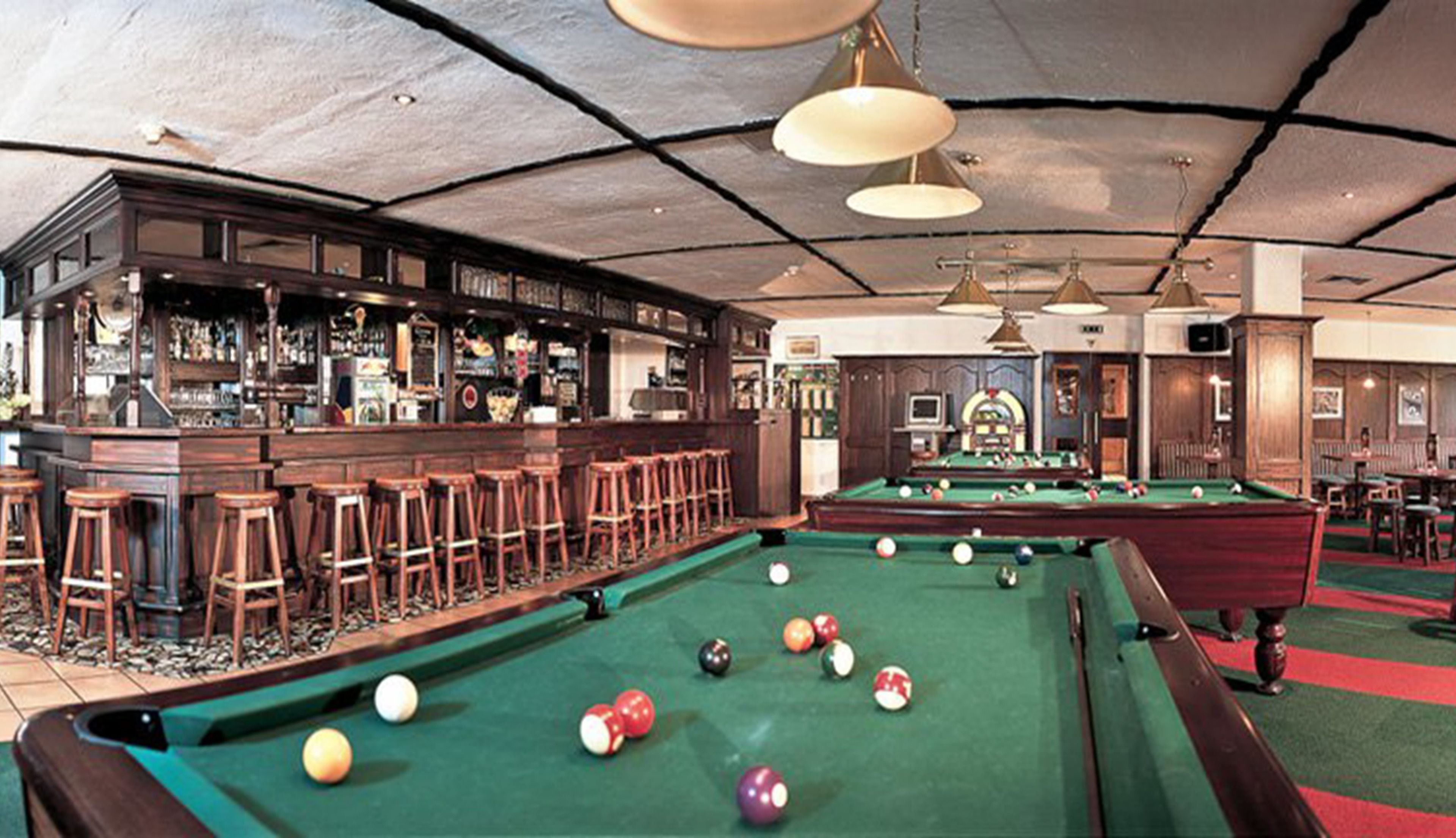 A bar area with a pool table, stools, and a bar counter.