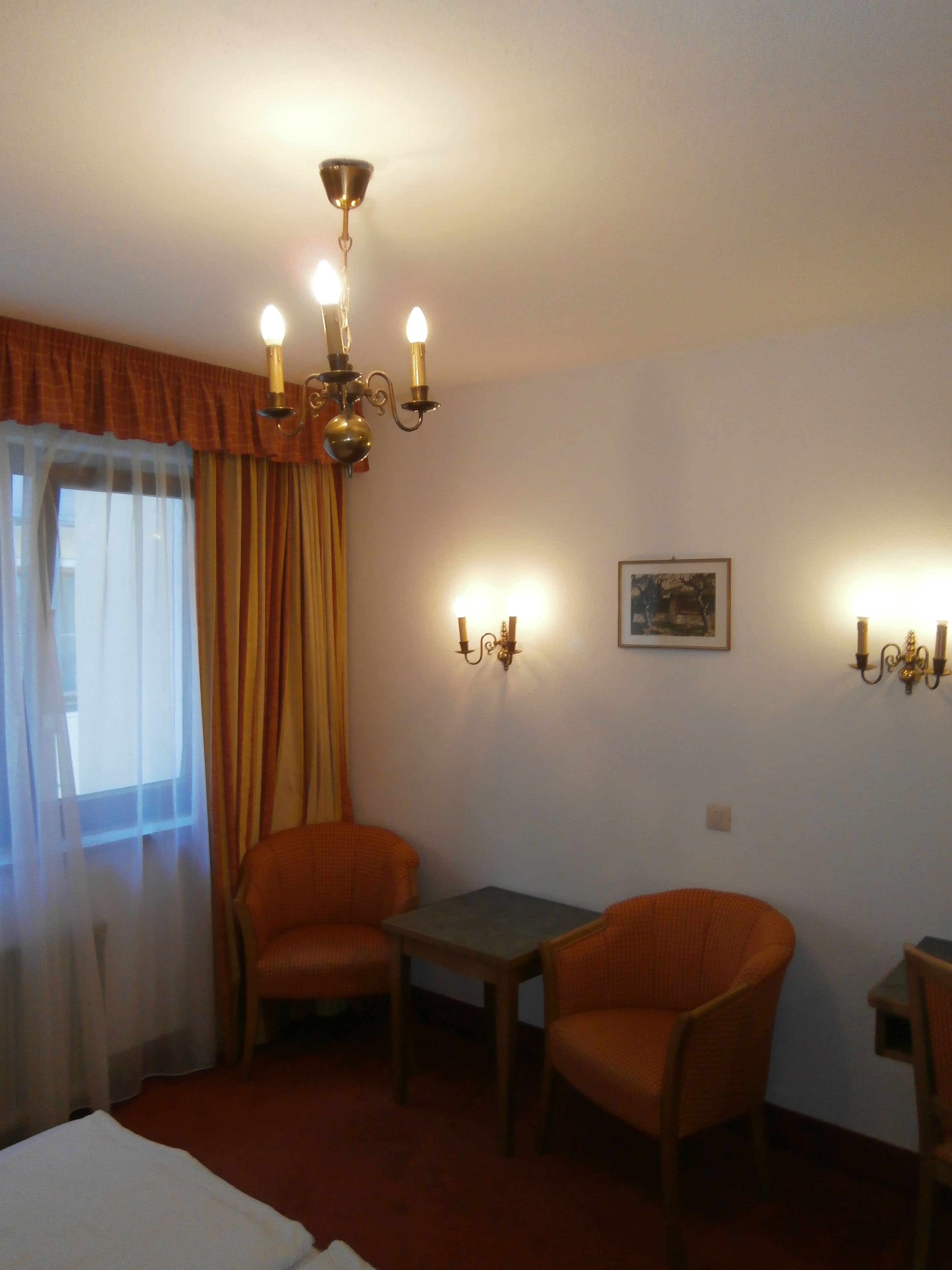 Ein Hotelzimmer mit zwei orangefarbenen Sesseln, einem kleinen Tisch, einem Bett und einer Kristallleuchtre.