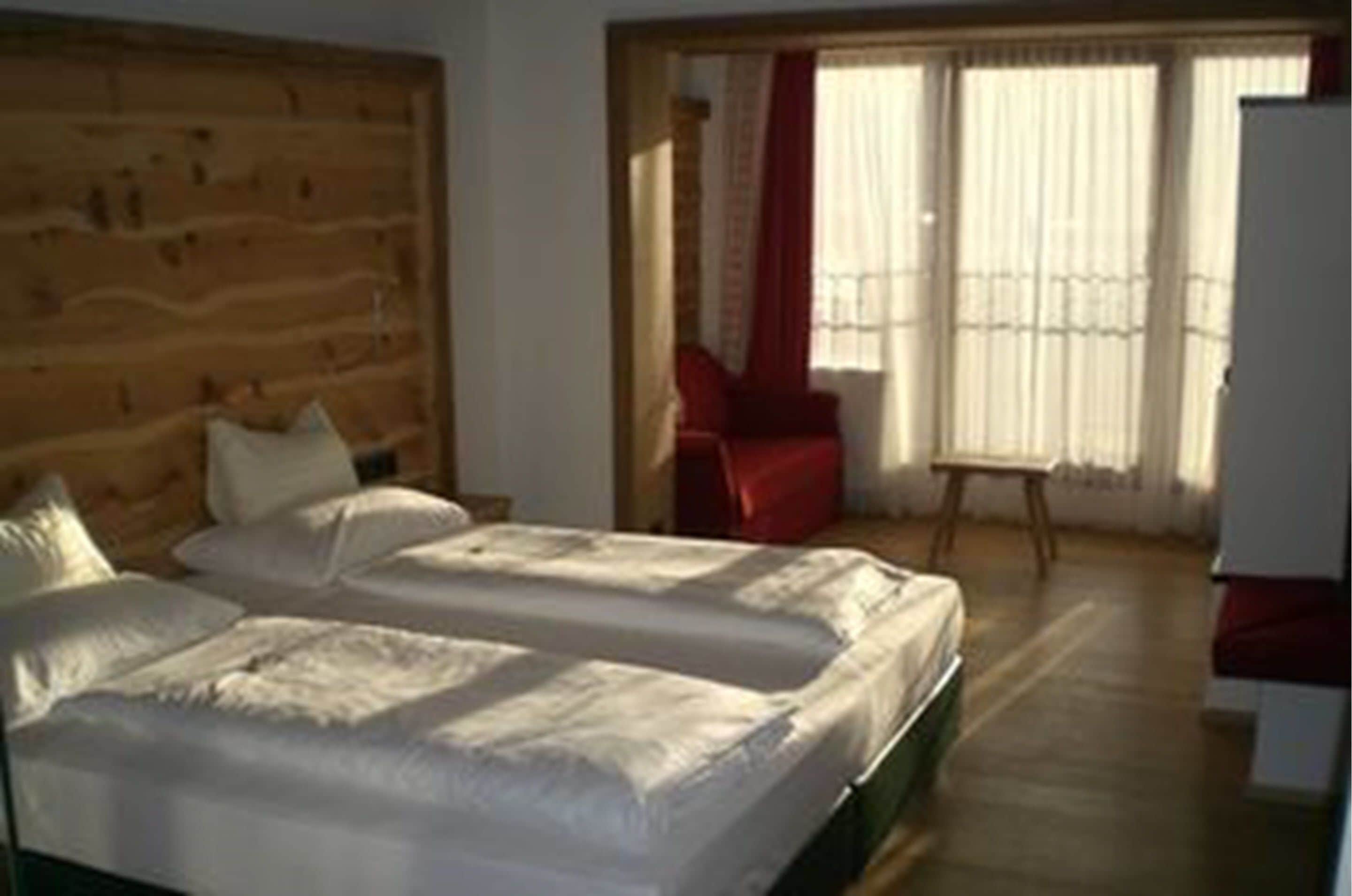 A room with two beds, a wooden headboard, a red chair, and a window with curtains.