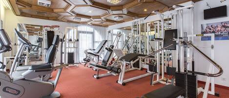 Un gimnasio con diverso equipo de ejercicio, piso de moqueta roja y diseño de techo de madera.