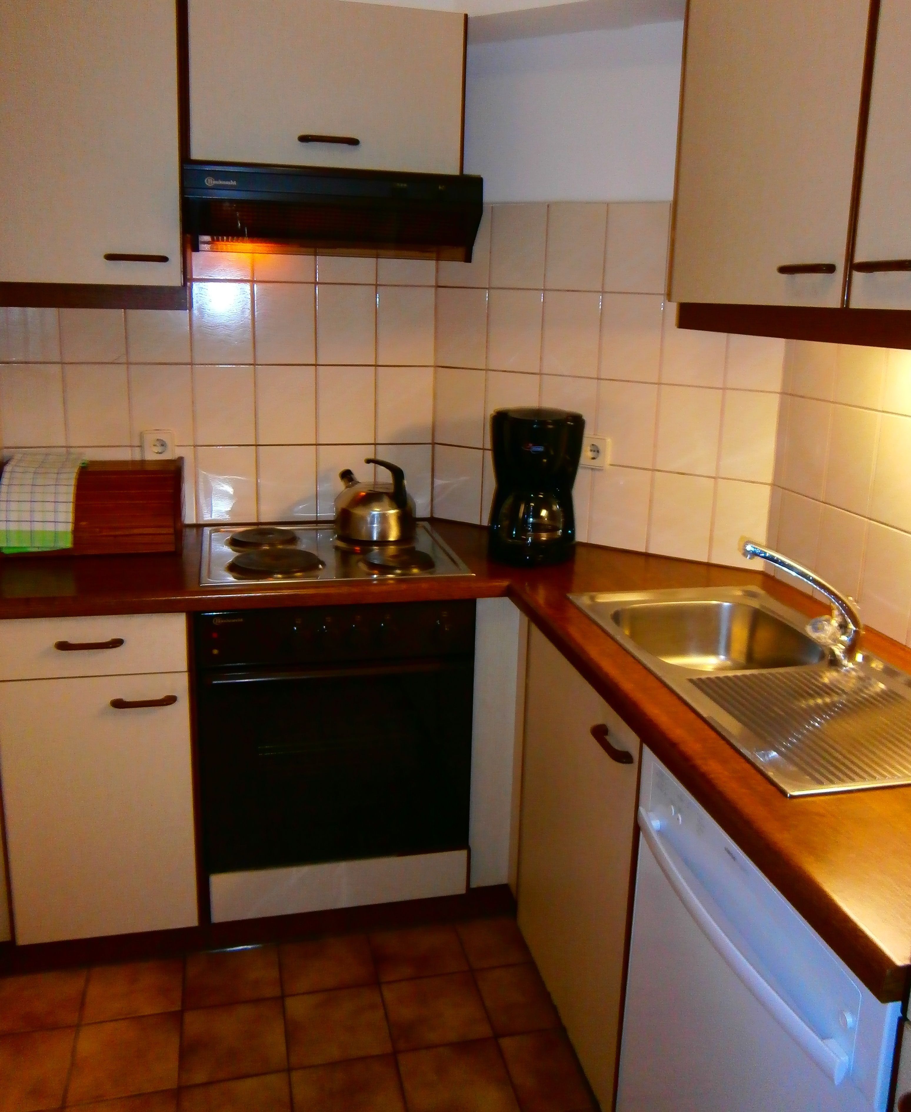A compact kitchen with white cabinets, a black stove, a coffee maker, and a dishwasher.