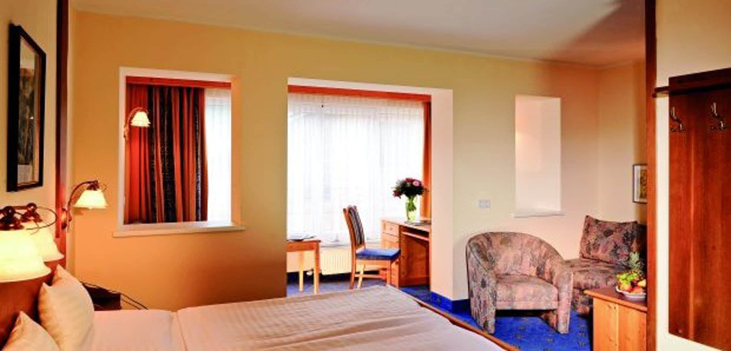 A hotel room with a bed, a desk, a chair, and a sofa.