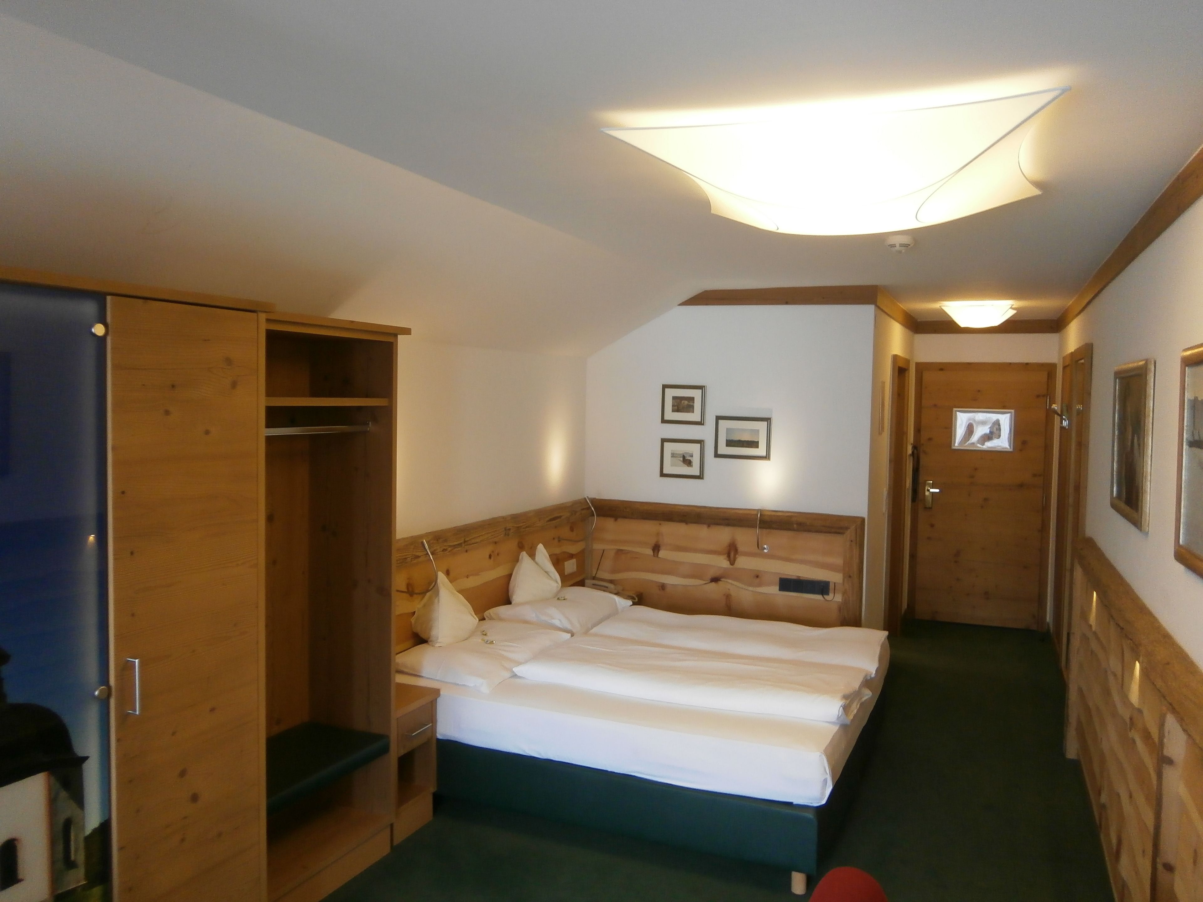 Una habitación pequeña y acogedora con cama, un armario de madera y una puerta que da a otra habitación.