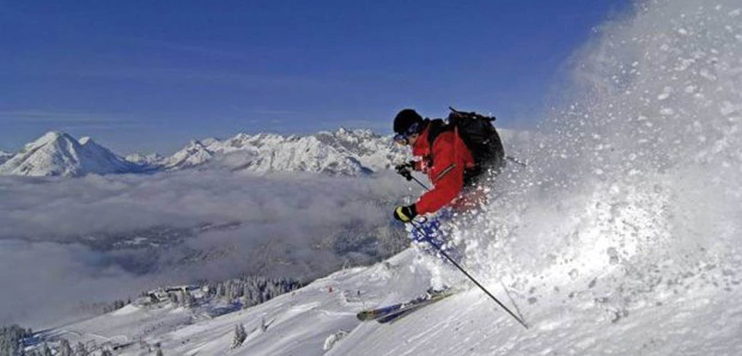 Un skieur sur une pente enneigée, avec une chaîne de montagnes en arrière-plan.