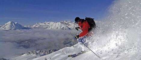 Un skieur sur une pente enneigée, avec une chaîne de montagnes en arrière-plan.
