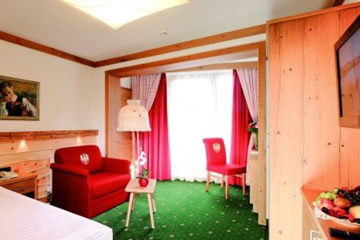 Une chambre d’hôtel avec un lit, un fauteuil rouge, une petite table avec une lampe et un panier de fruits.