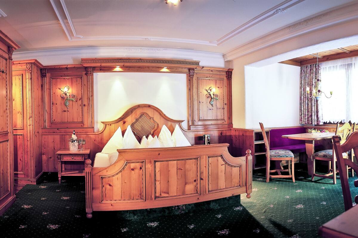 Une chambre de style traditionnel avec un lit en bois, un coin repas comprenant une table et des chaises, et une fenêtre avec des rideaux.