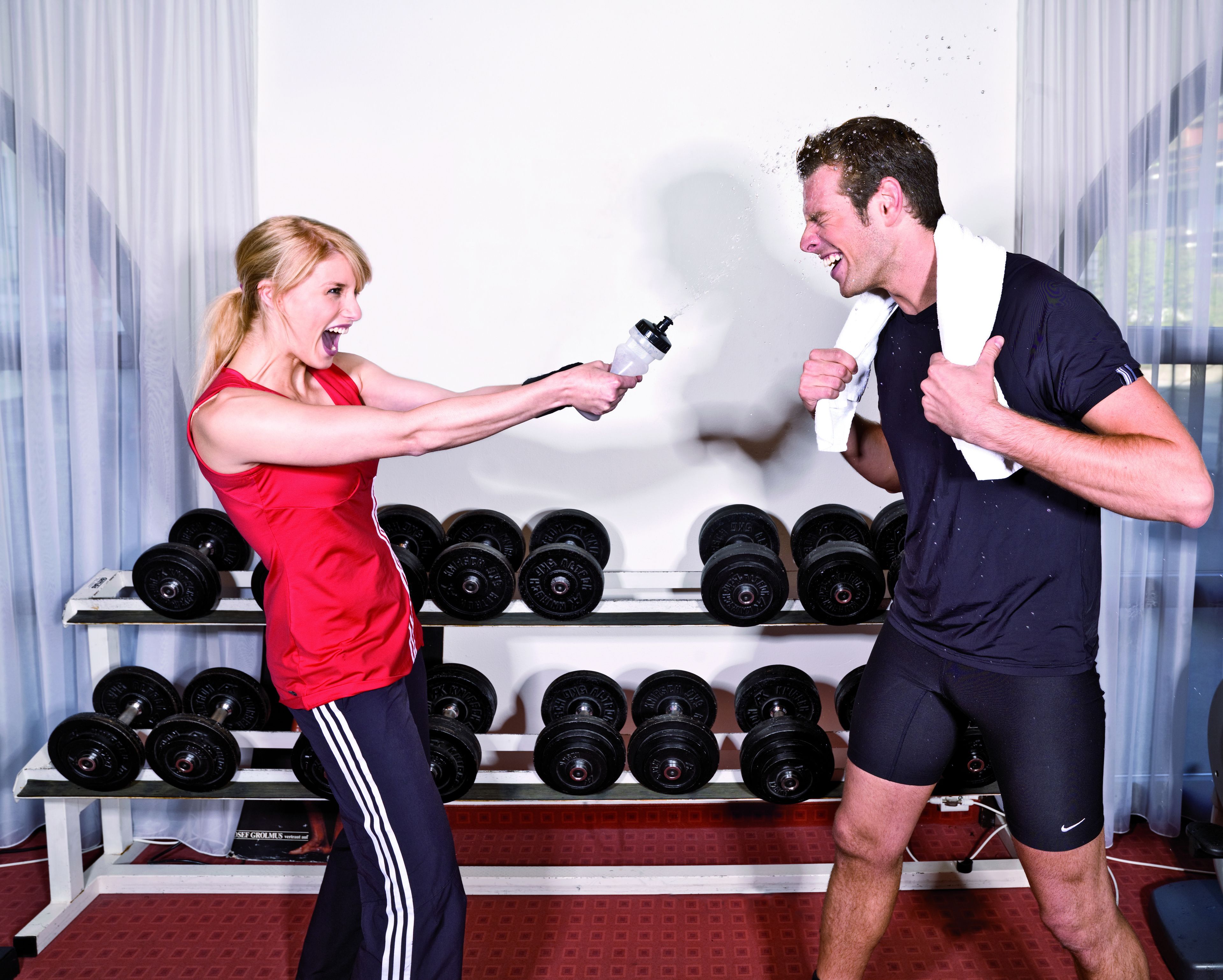 Une salle de sport où une femme et un homme font de l’exercice, entourés d’haltères et d’appareils de musculation.