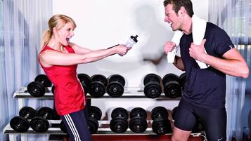 Une salle de sport où une femme et un homme font de l’exercice, entourés d’haltères et d’appareils de musculation.