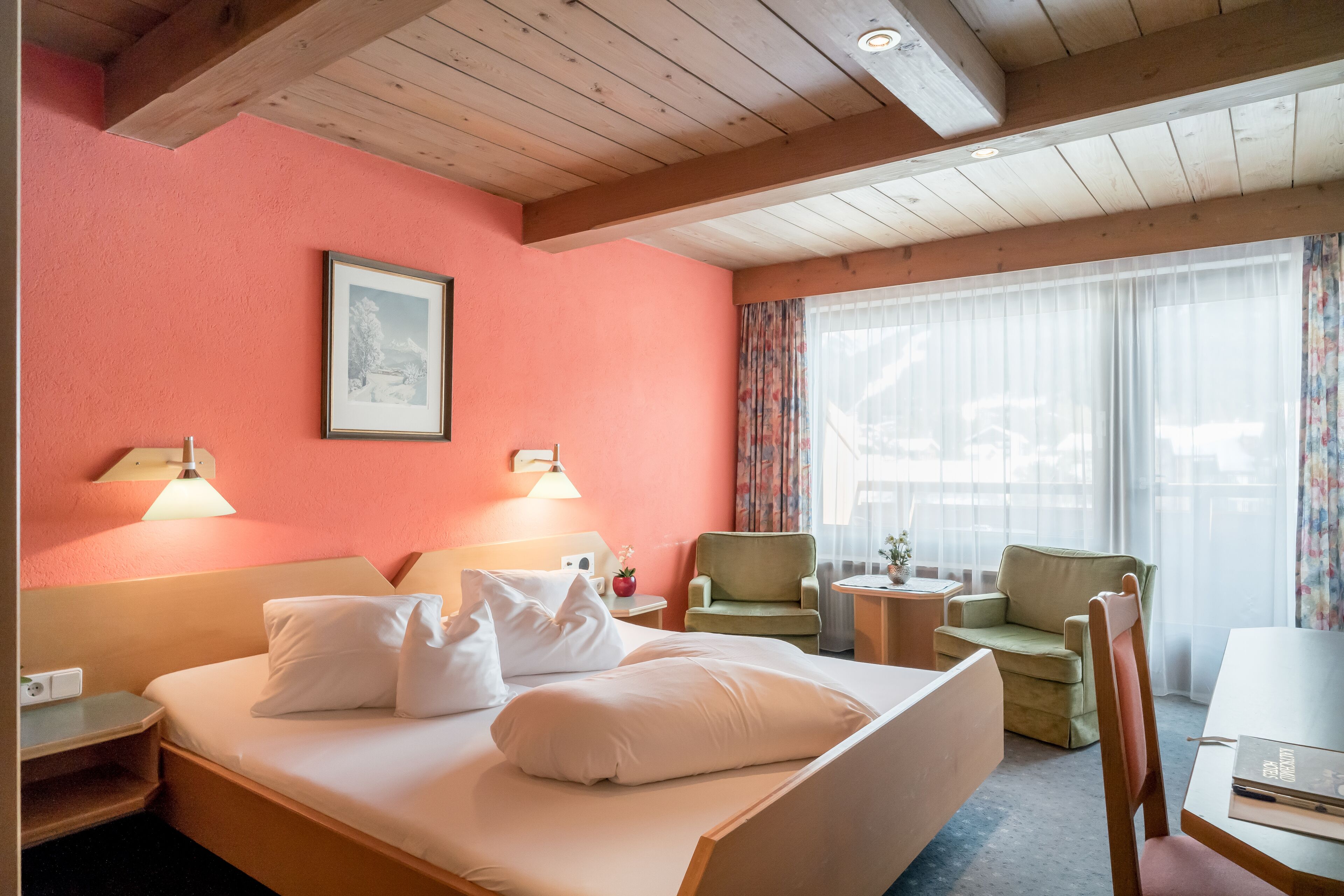 Una habitación de hotel con cama, dos sillas, una mesita y una ventana con cortinas.