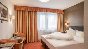 A hotel room with a bed, a desk with a chair, a lamp, and a window with curtains.
