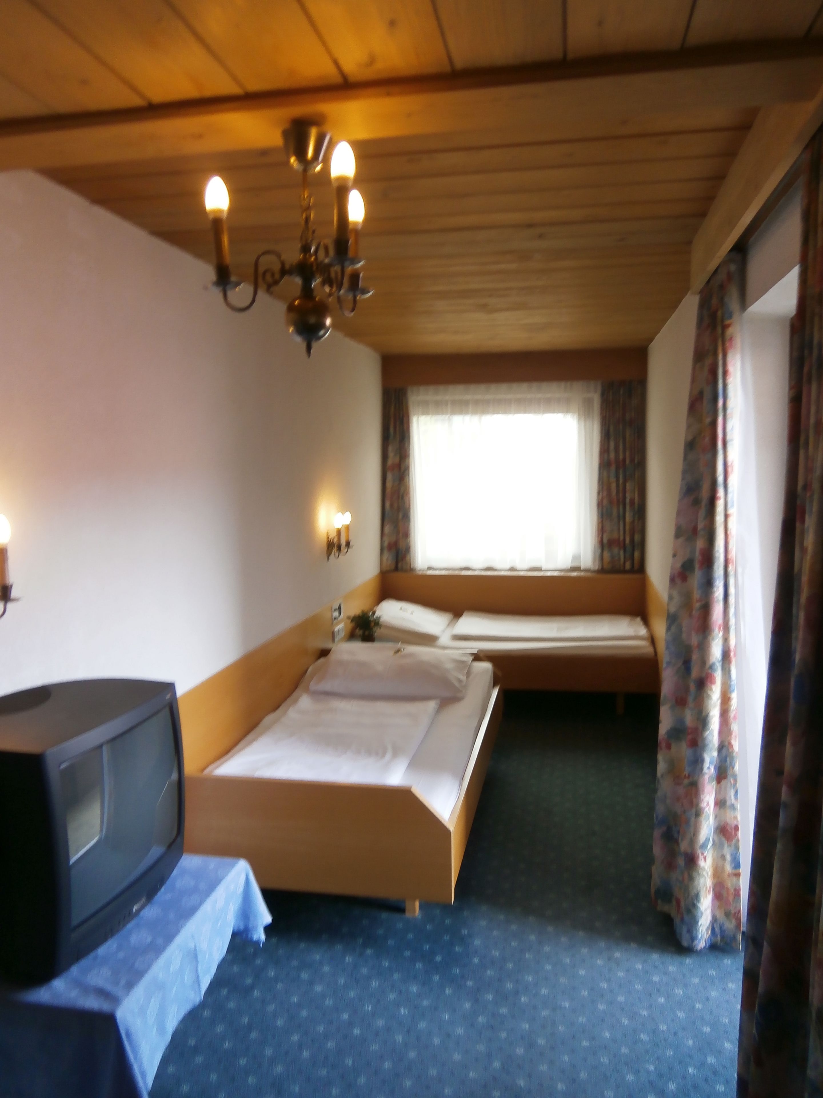 Een hotelkamer met twee bedden, een televisie, een kroonluchter en een raam met gordijnen.