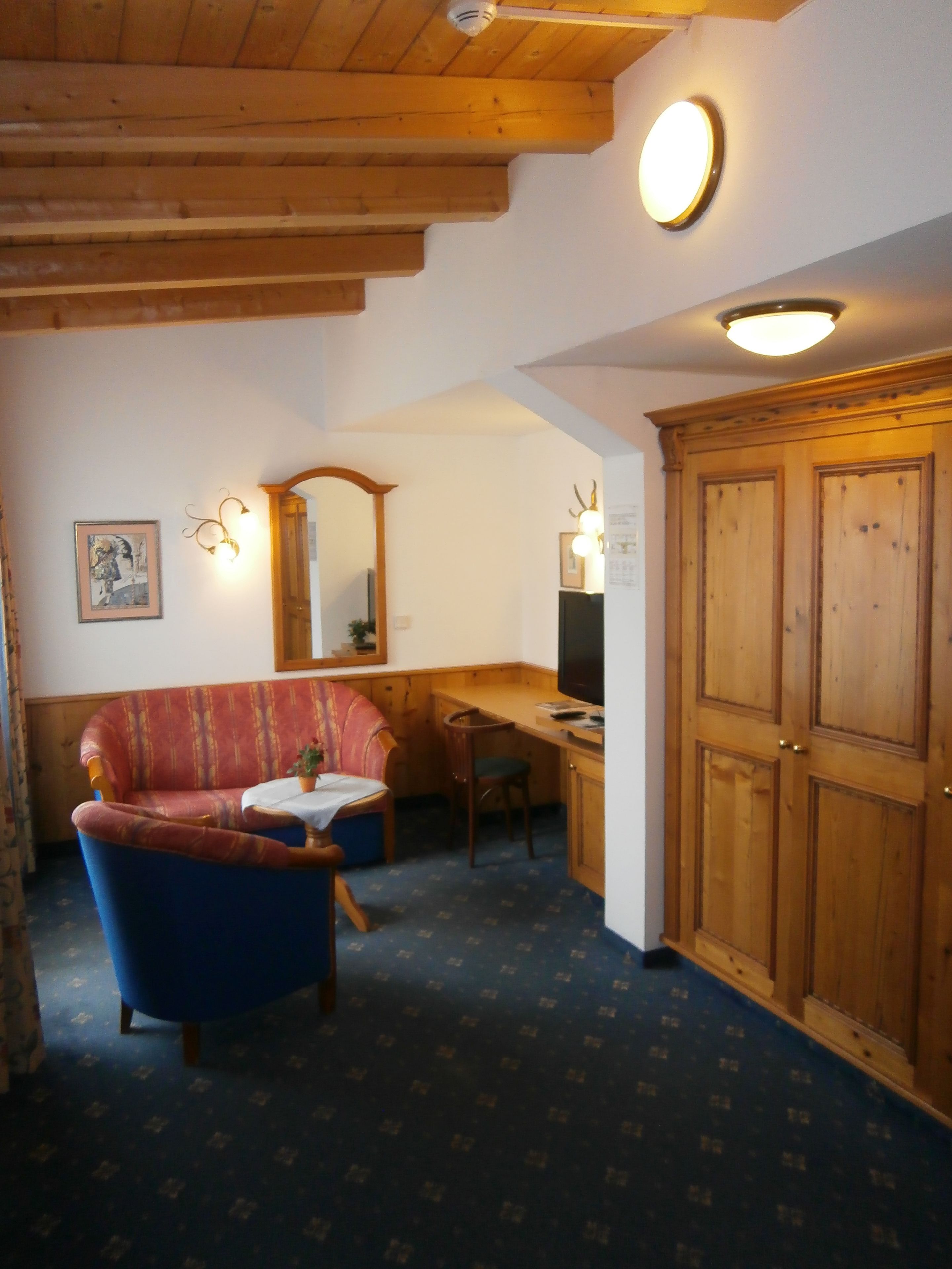 A cozy room with a wooden ceiling, a blue armchair, a small table with a plant, and a wooden cabinet.