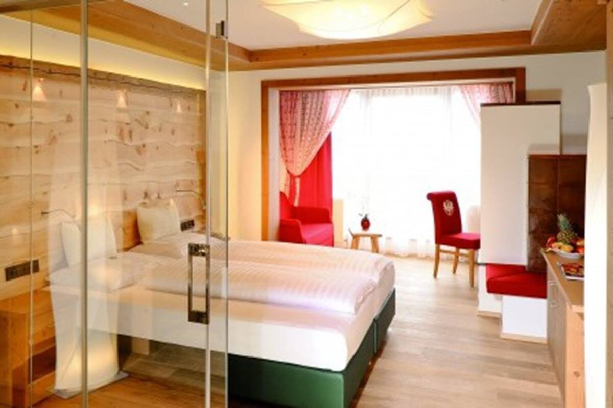 Une chambre moderne avec une cloison en verre, un lit, un fauteuil rouge et une petite table sur laquelle se trouvent des fruits.