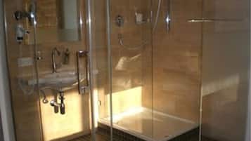 Zona de ducha con mampara de vidrio, bañera, lavamanos y espejo.