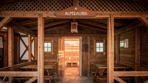 Interior de una cabaña de madera con piso de piedra, bancos de madera y un cartel que dice 'ALMSAUNA'.