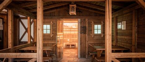 A wooden cabin interior with a stone floor, wooden benches, and a sign reading "ALMSAUNA".