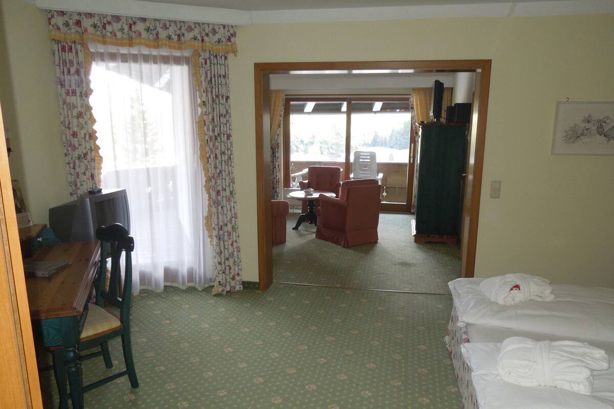 A hotel room with a bed, a desk with a chair, a small table, and a window with curtains.