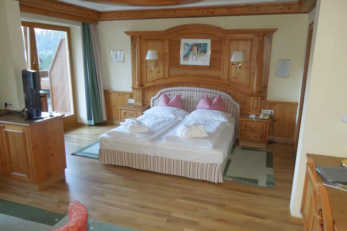 A spacious bedroom with a large bed, wooden headboard, bedside tables with lamps, and a view through a window.