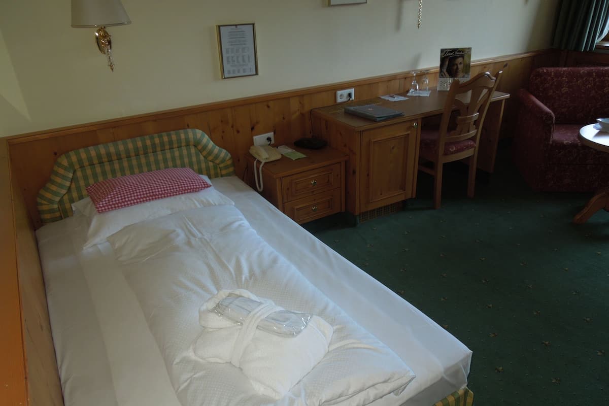 A hotel room with a bed, a desk, a chair, and a small table.