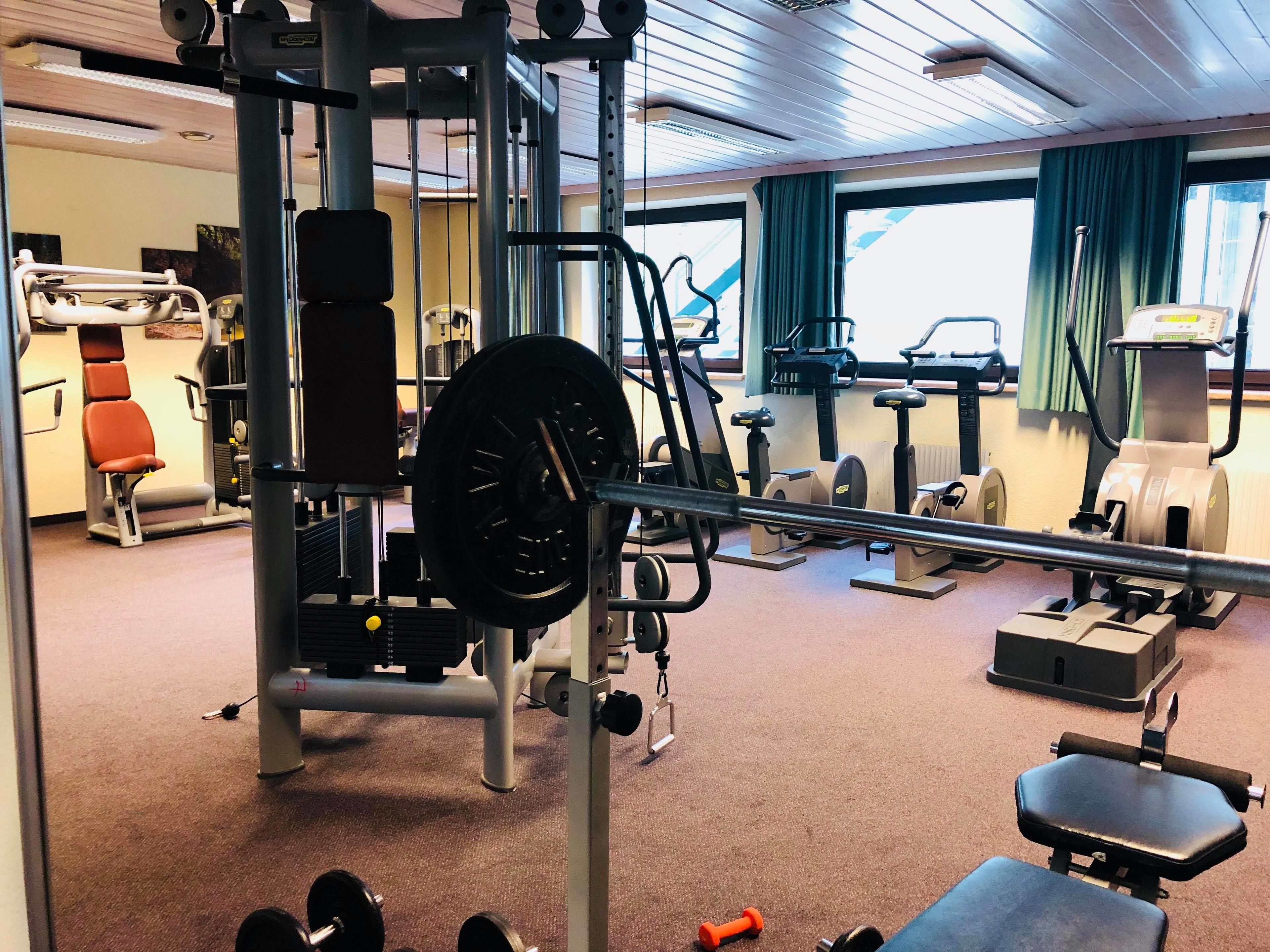 A gym with various exercise equipment, including a squat rack, dumbbells, and cardio machines.