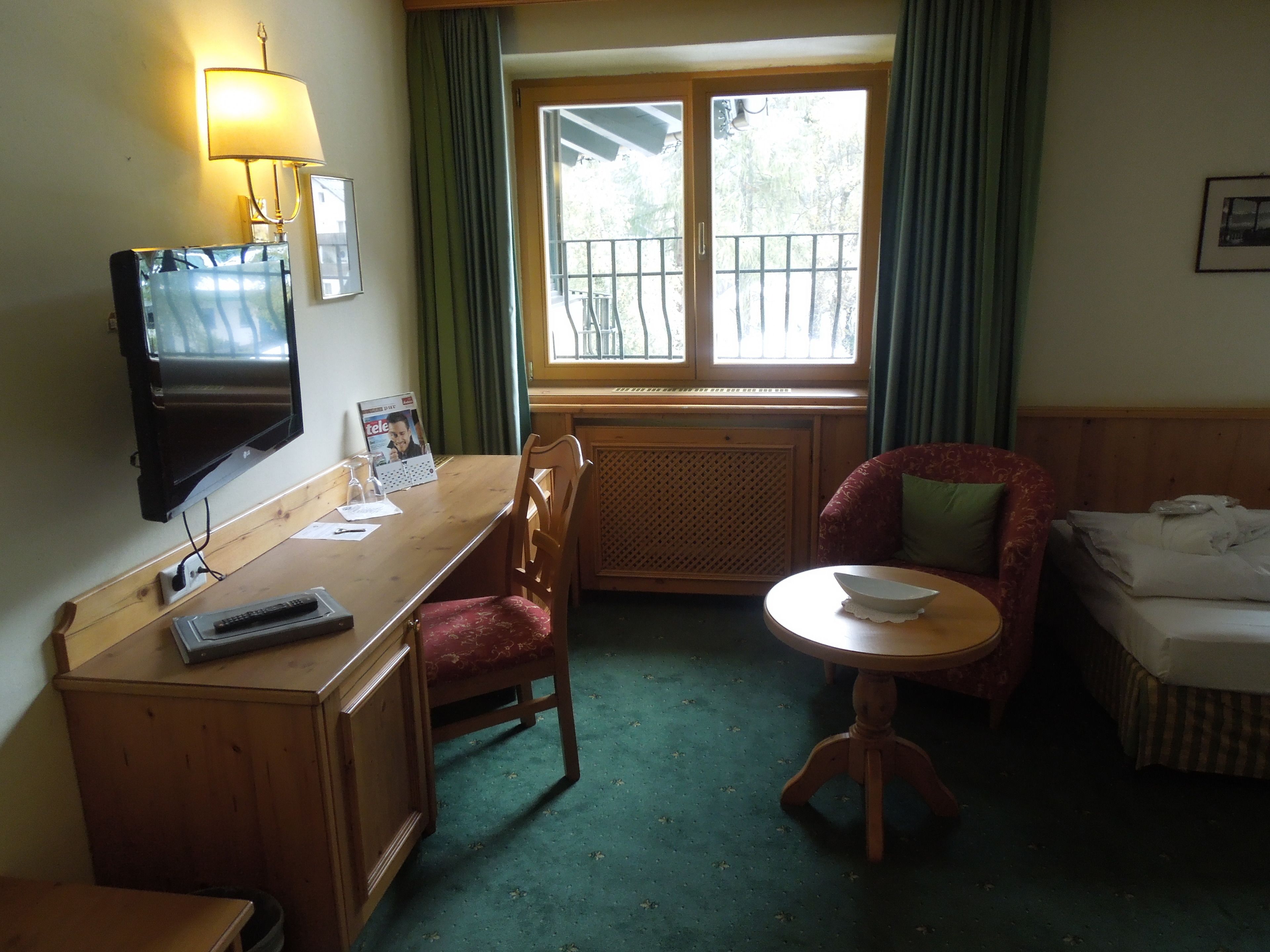 Habitación de hotel con escritorio de madera, televisor, silla, mesita redonda y cama.