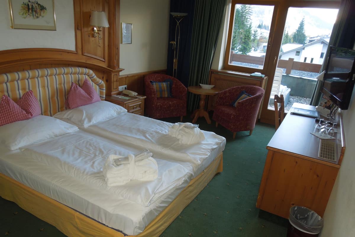 A hotel room with a large bed, two bedside tables, a desk with a computer, a chair, and a TV.