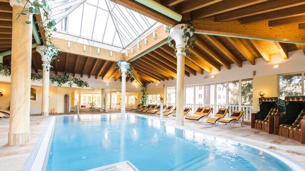 Una piscina interior con tragaluces, vigas de madera y tumbonas.
