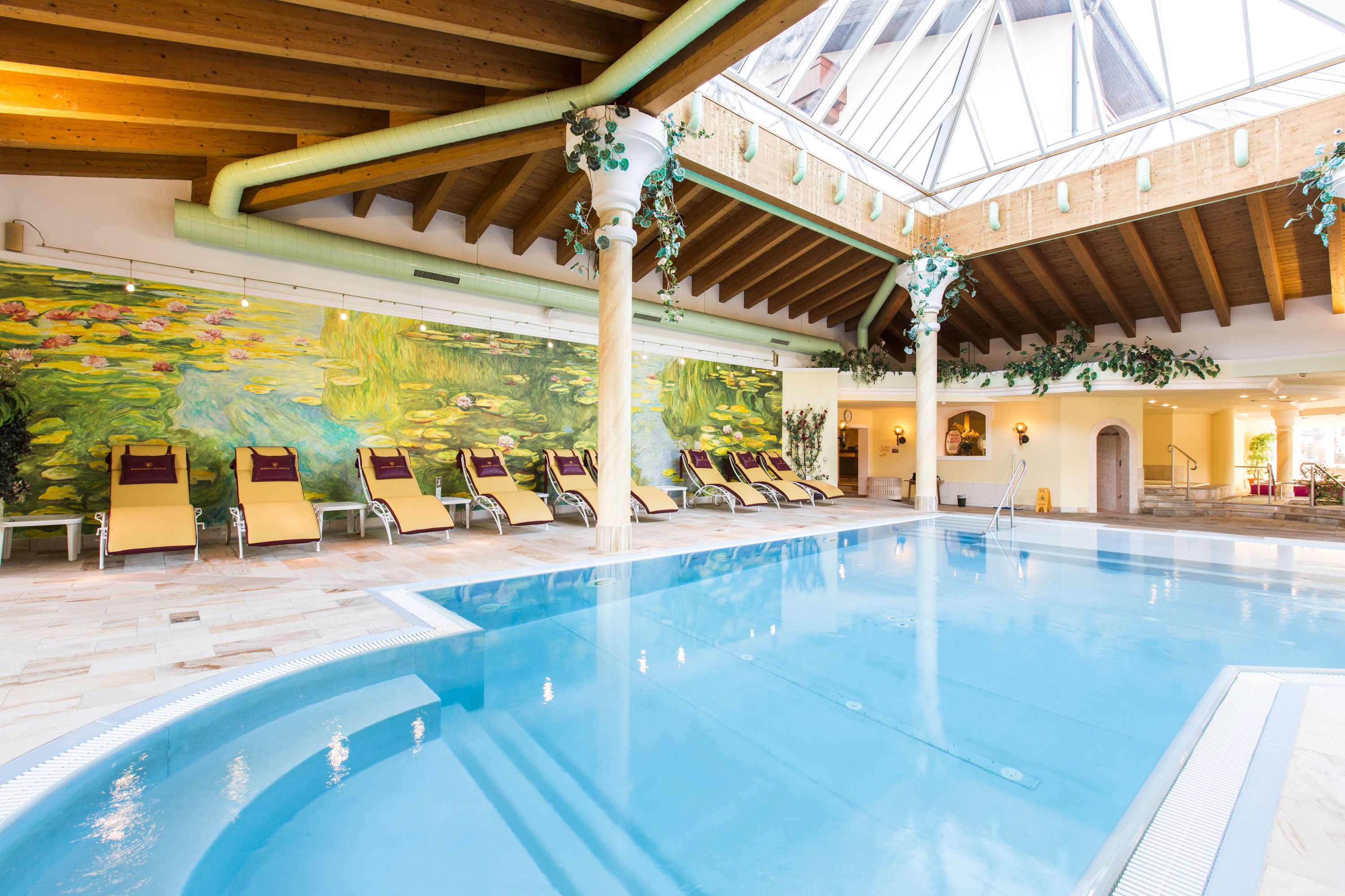 An indoor swimming pool with lounge chairs and a mural on the wall.