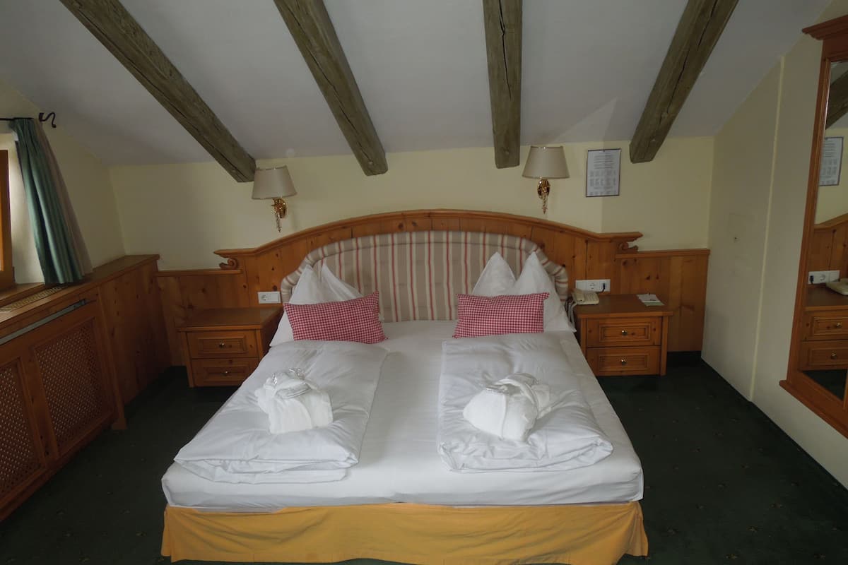 A double bed with white linens, two pillows, and a yellow skirt. There are two bedside tables with lamps, a wooden headboard, and a mirror on the wall.
