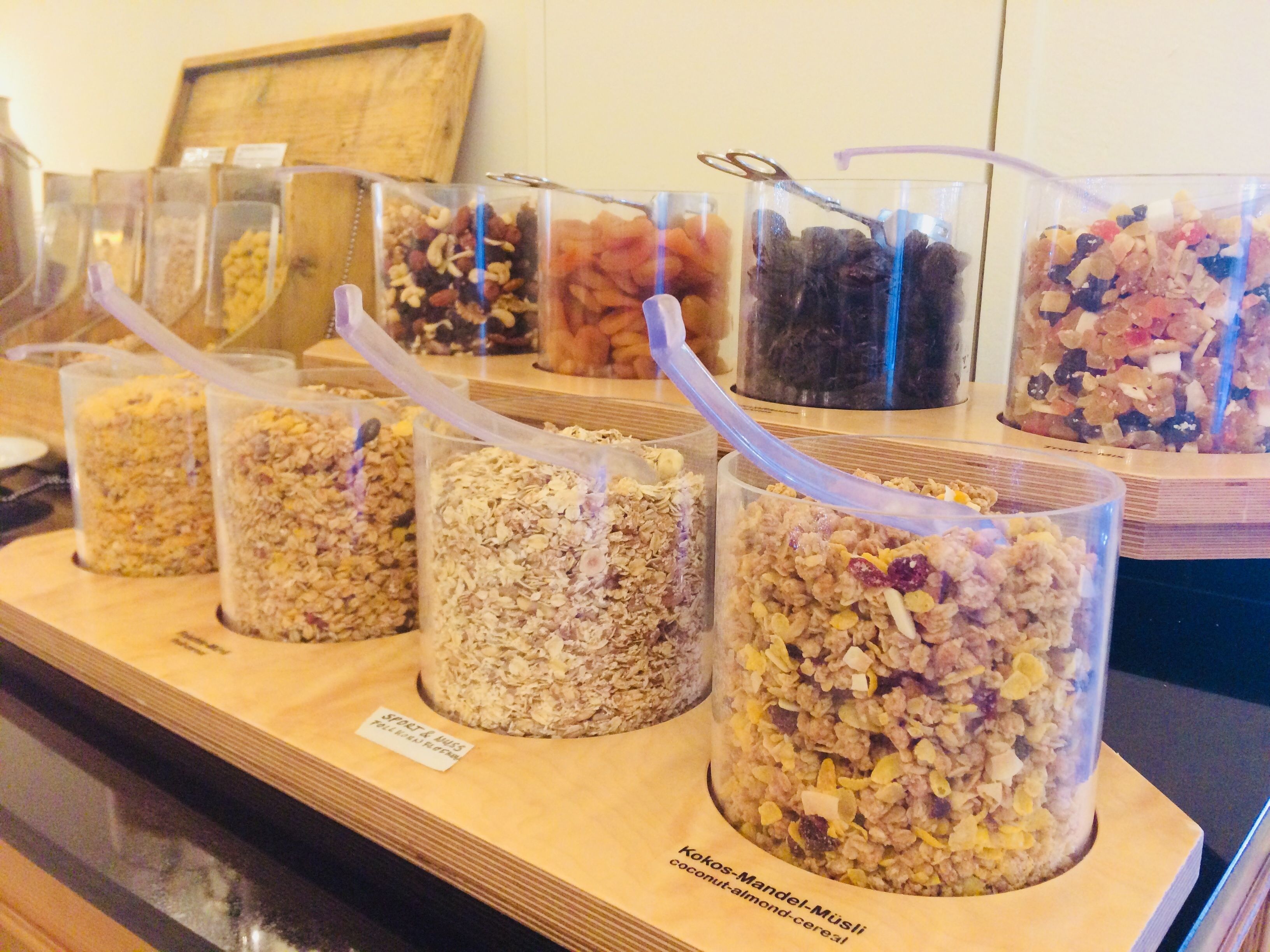 A display of various granola and cereal bars in transparent containers with spoons.