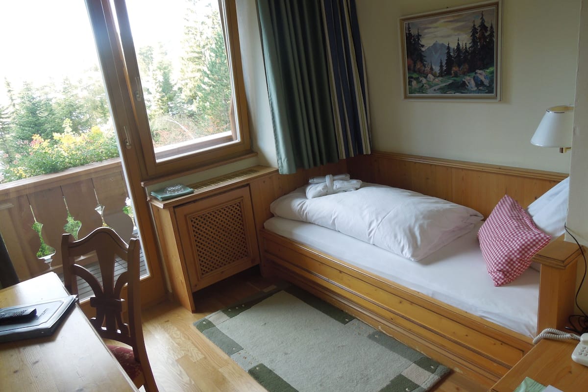 A small, cozy room with a bed, a desk, and a window with curtains.
