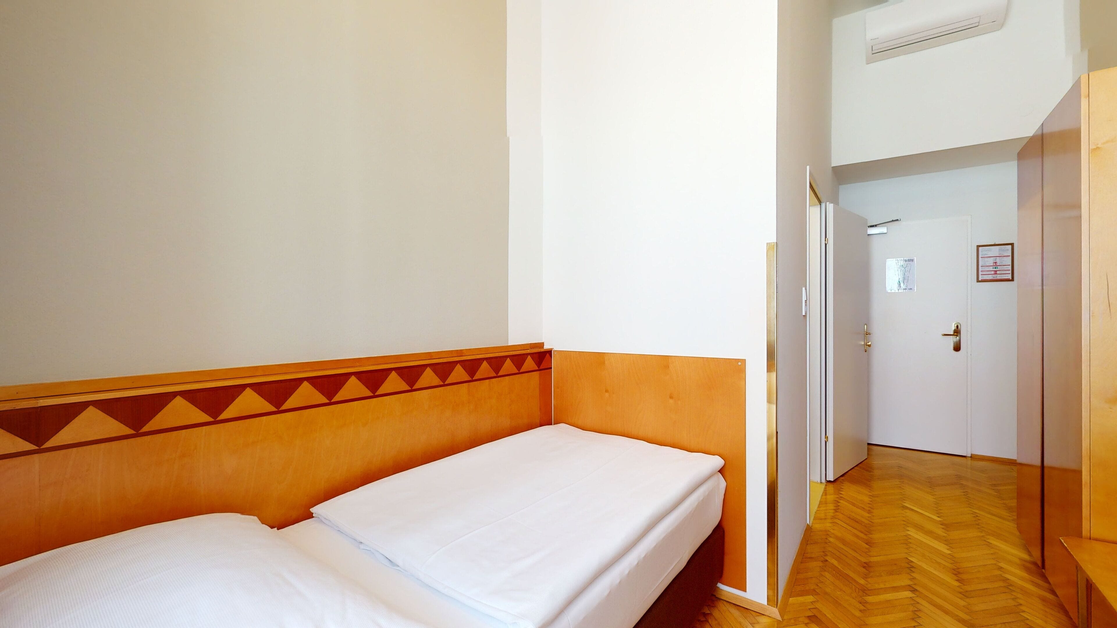 Een hotelkamer met een houten hoofdeinde, een bed met wit beddengoed, een houten vloer en een deur met een bordje.