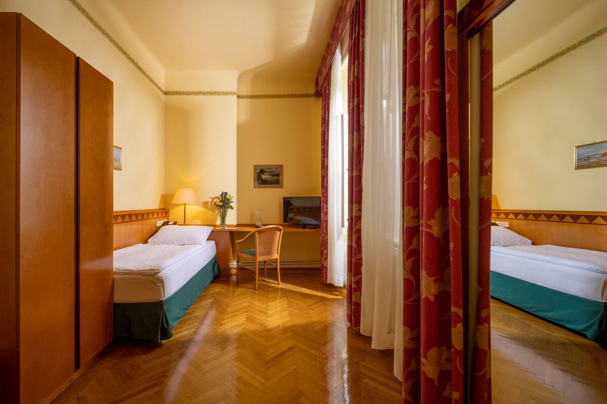 Ein Hotelzimmer mit zwei Betten, einem Schreibtisch, einem Stuhl, einer Lampe und einem Gemälde an der Wand.
