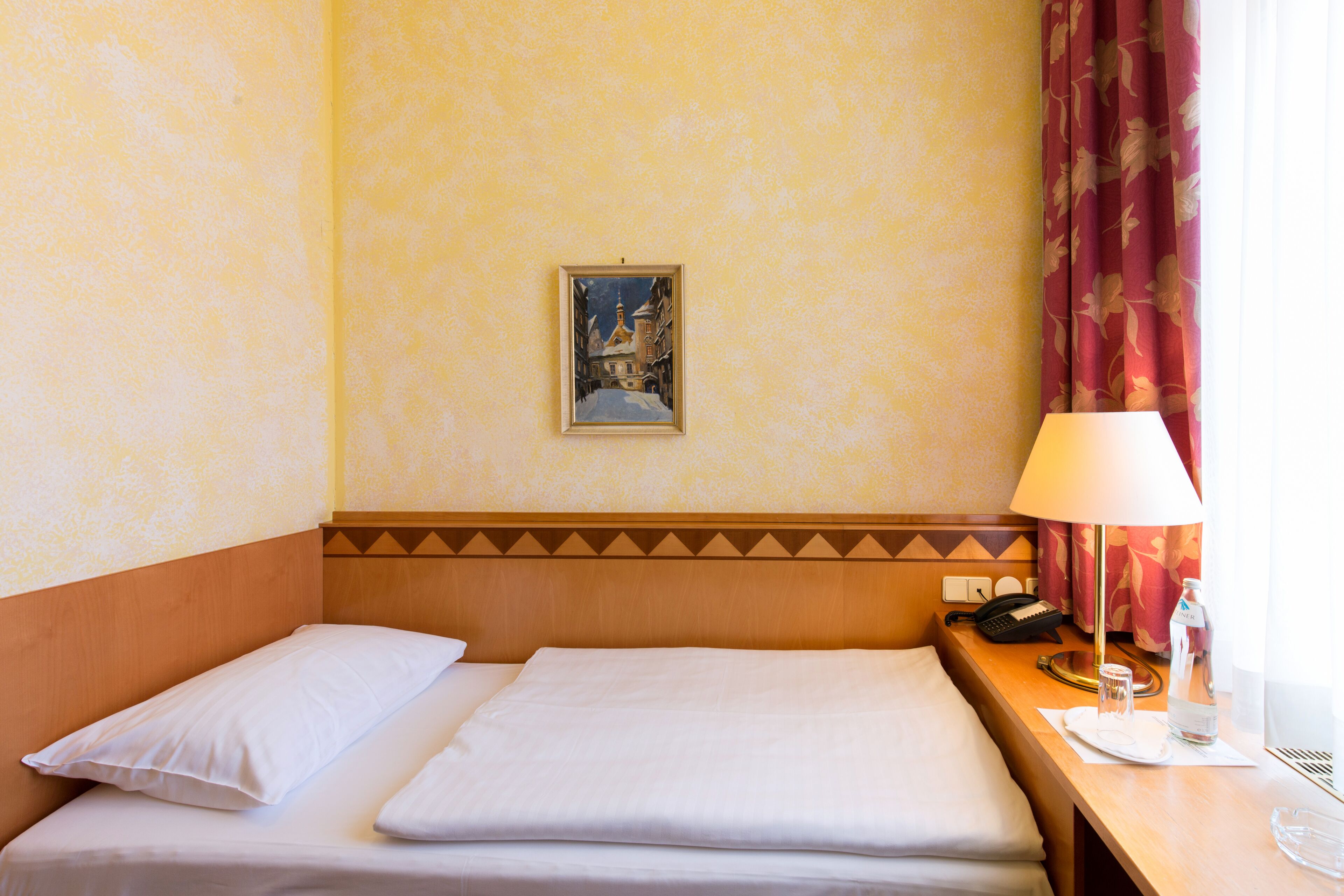 A hotel room with two beds, a painting on the wall, a lamp, a phone, and a bottle of water on the nightstand.