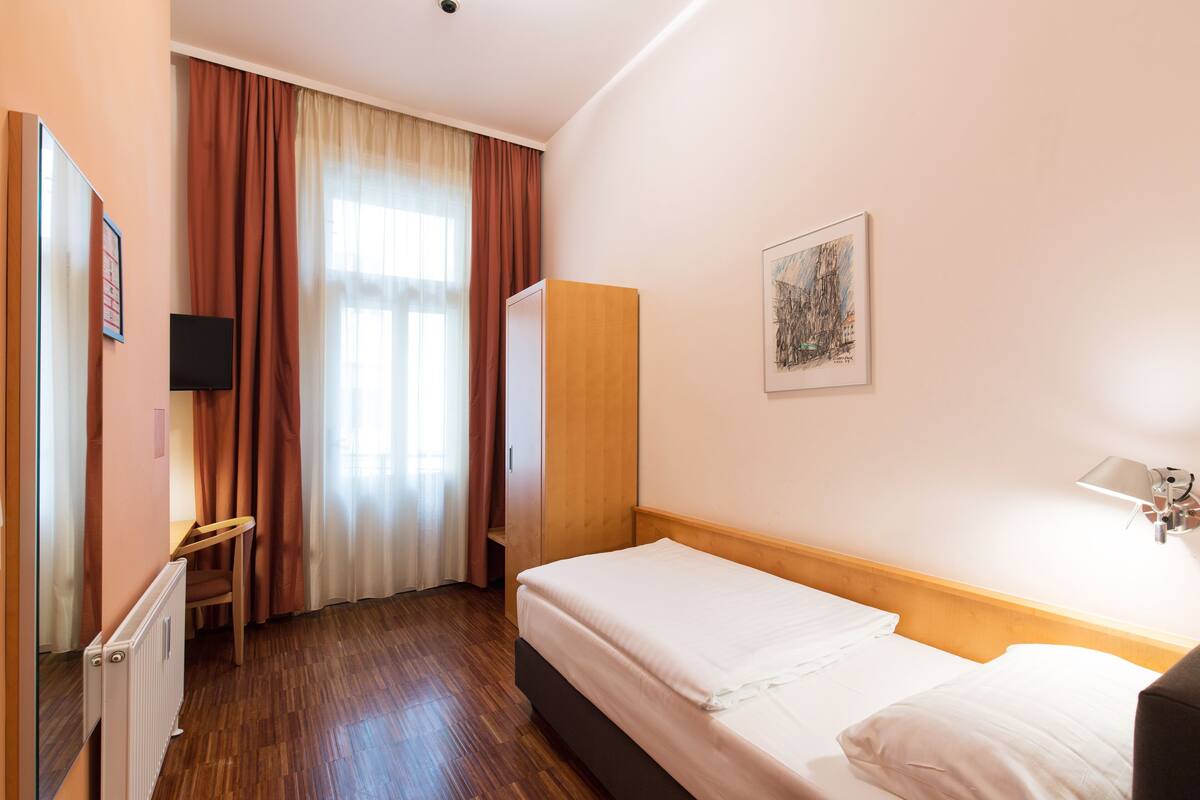 Ein Hotelzimmer mit Bett, Schreibtisch, Stuhl, Kleiderschrank und einem Bild an der Wand.