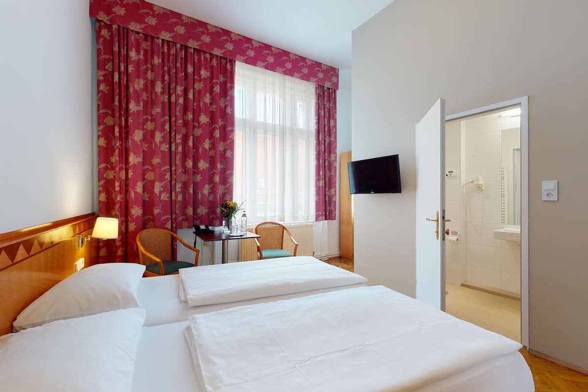 Ein Hotelzimmer mit zwei Betten, einem Schreibtisch mit Stuhl, einem Fernseher und einer Badezimmertür.