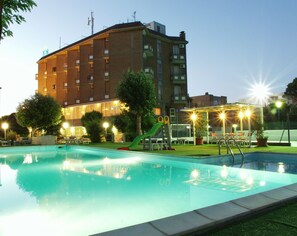 A swimming pool with a slide, surrounded by a fenced area with chairs and tables, and a multi-story building in the background. - Family Hotel Marina Beach (Ravenna)