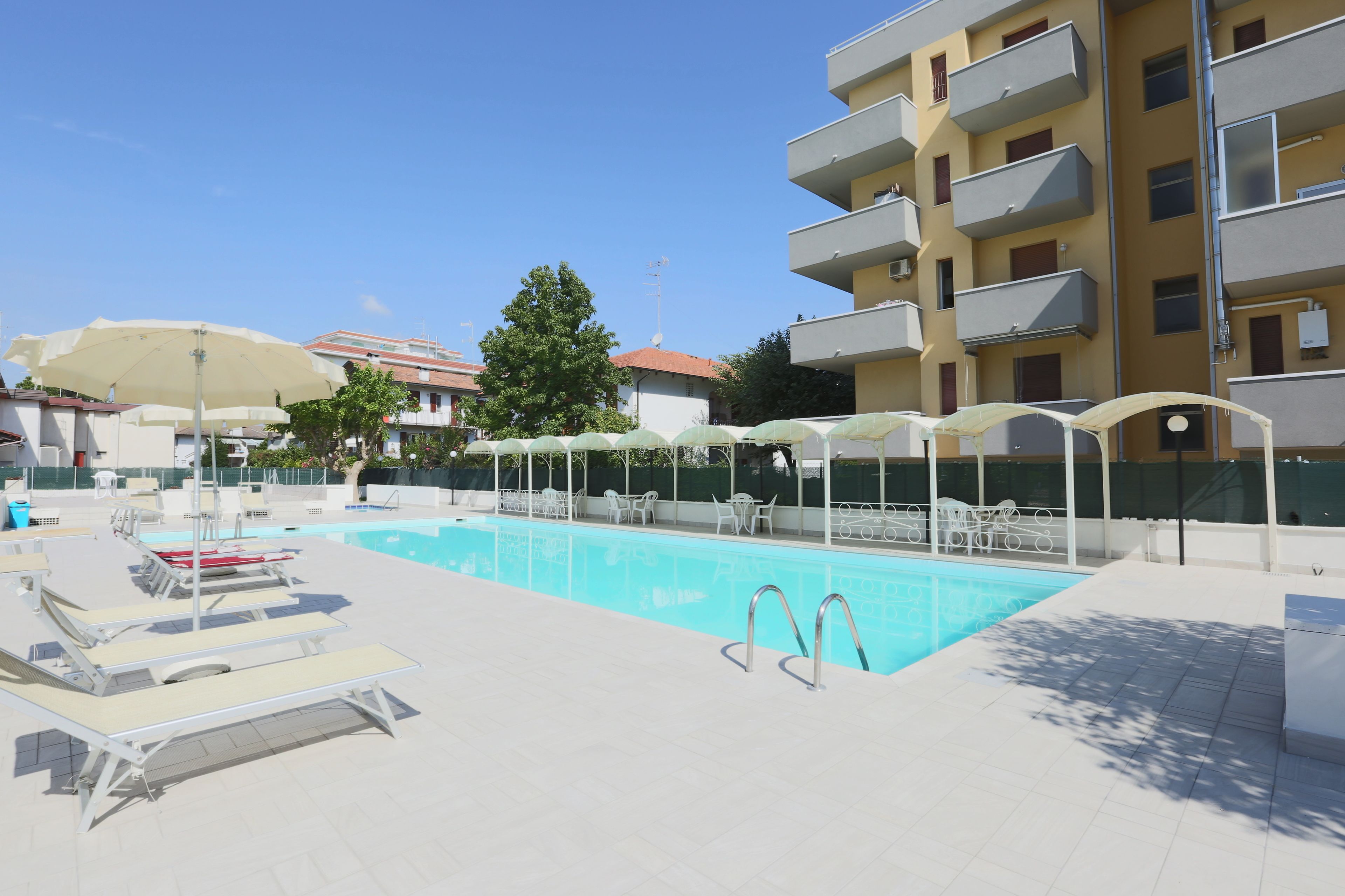 A swimming pool area with lounge chairs and umbrellas, surrounded by a building with balconies.
