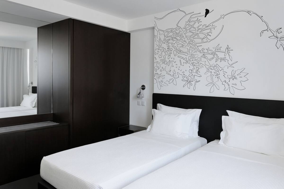 A modern hotel room with a large bed, dark wood wardrobe, and a wall-mounted artwork of a bird and flowers.