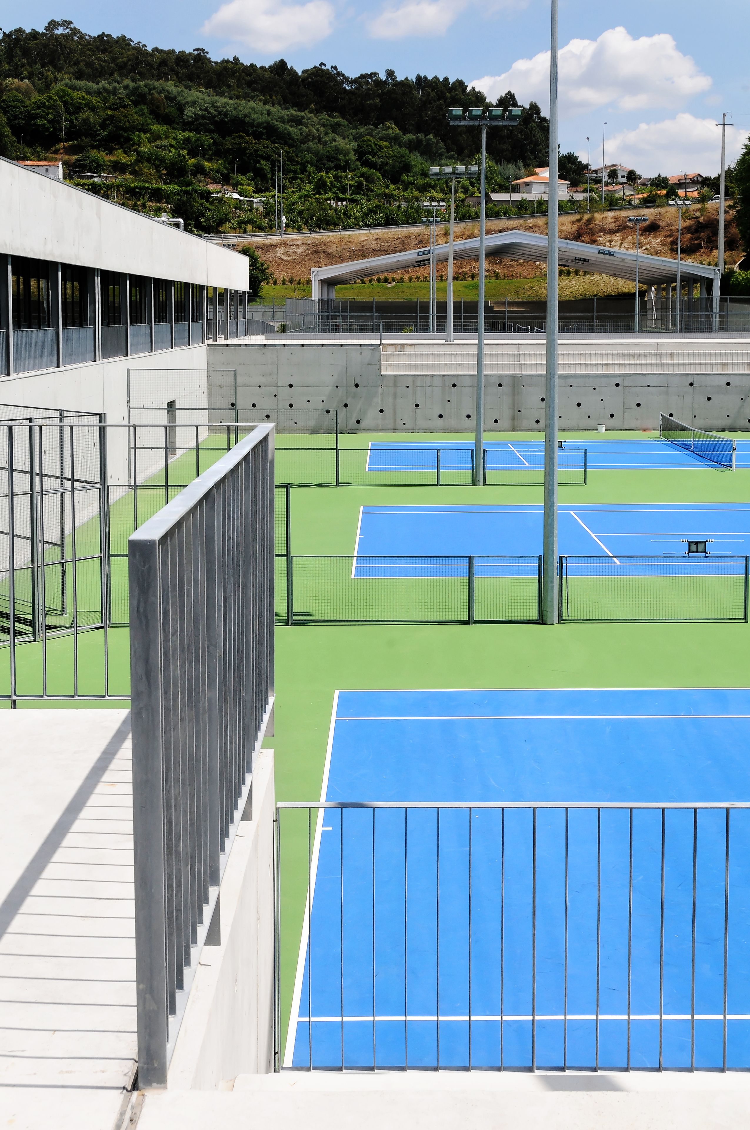 A tennis court with multiple courts, a fence, and a building in the background.