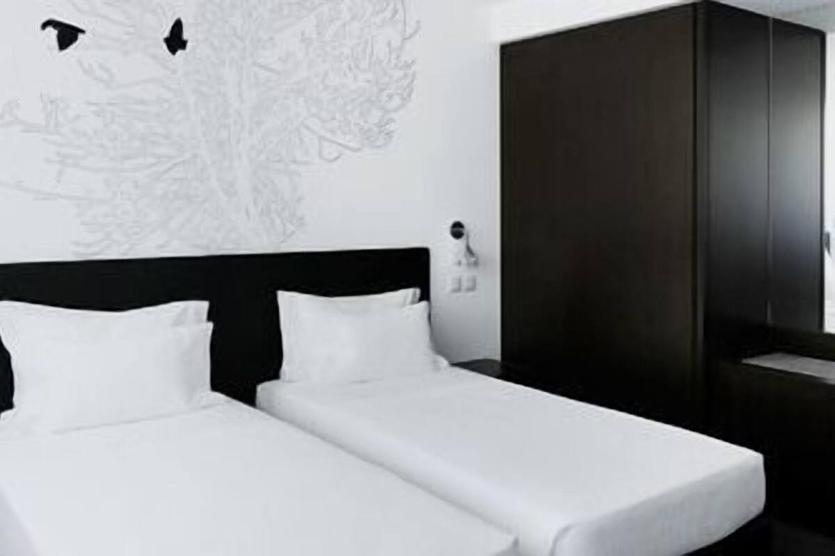 A hotel room with two single beds, a dark wardrobe, and a window with a view.