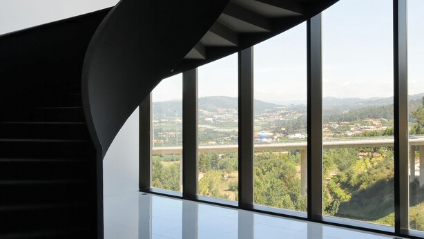 A modern interior with a spiral staircase, large windows, and a view of a landscape. - Open Village Sports Hotel & SPA Club (Guimarães)