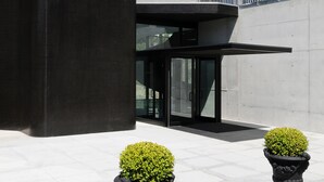A modern building with a flat roof, large windows, and a balcony. There are two potted plants in front. - Open Village Sports Hotel & SPA Club (Guimarães)