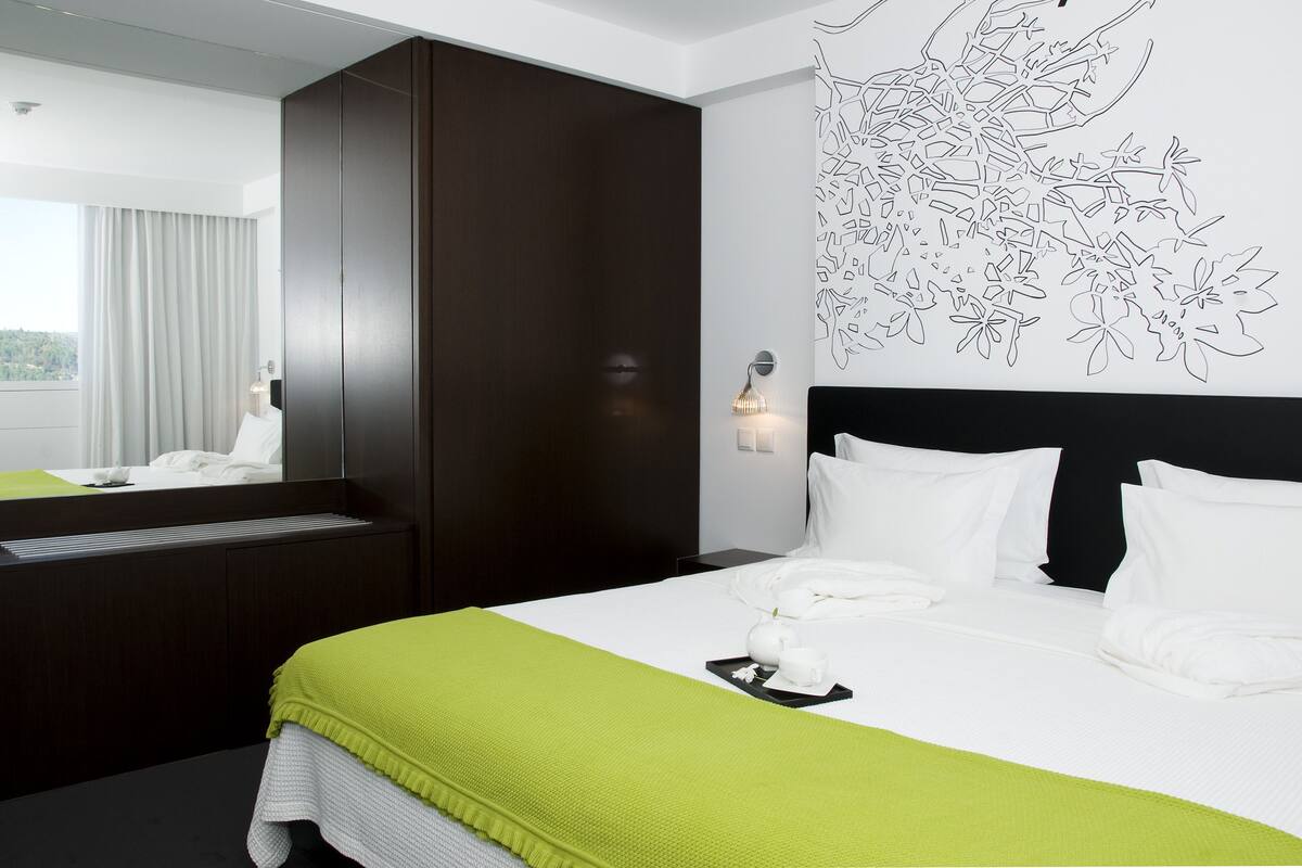 A hotel room with a large bed, a dark wardrobe, a wall-mounted light, and a window with curtains.